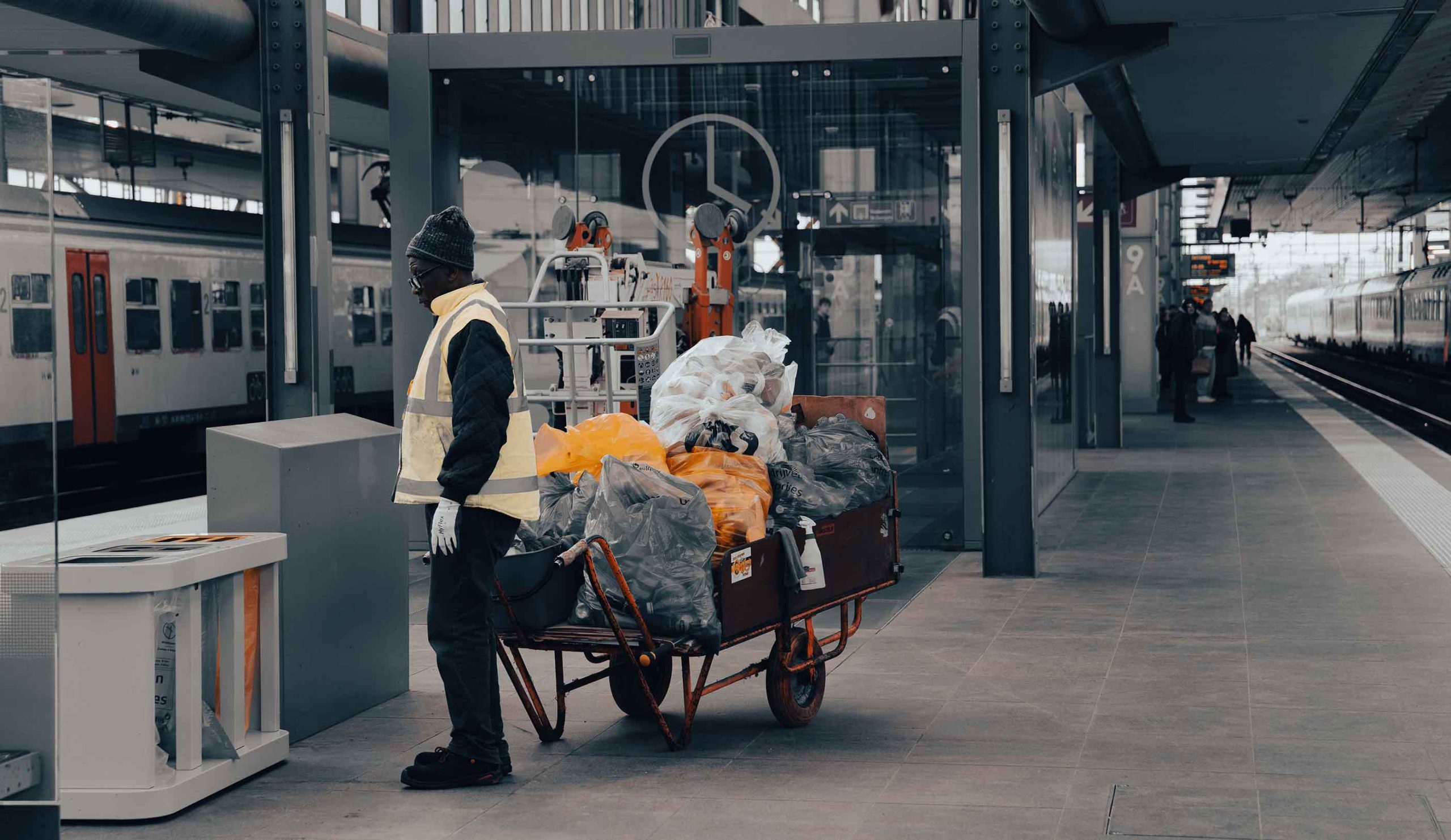 A man maneuvers a cart stacked with multiple items, moving through a crowded space.