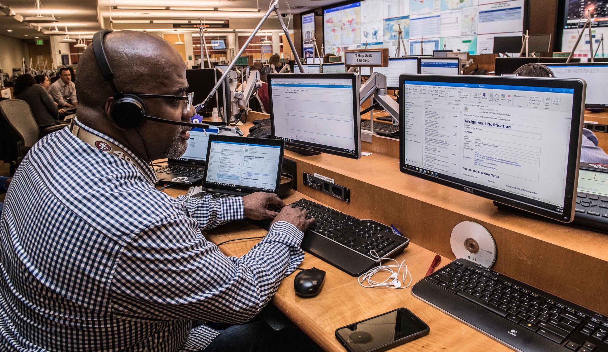 A man wearing a headset is focused on his computer screen, engaged in work-related tasks