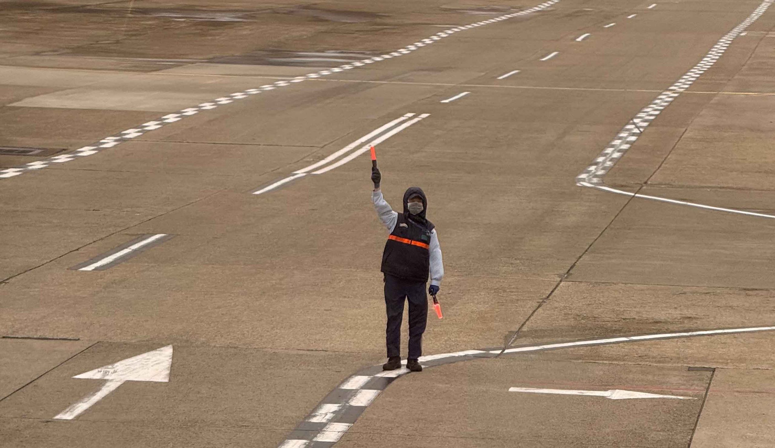 A man stands on the runway holding a red flag, signaling for attention or caution